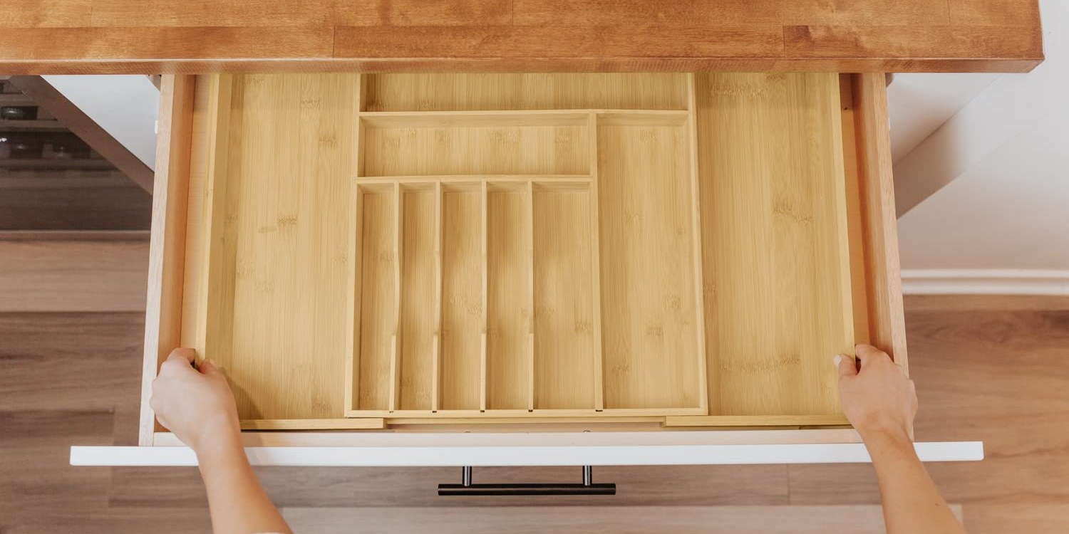 Hands spreading an expandable bamboo drawer organizer out to the drawer walls