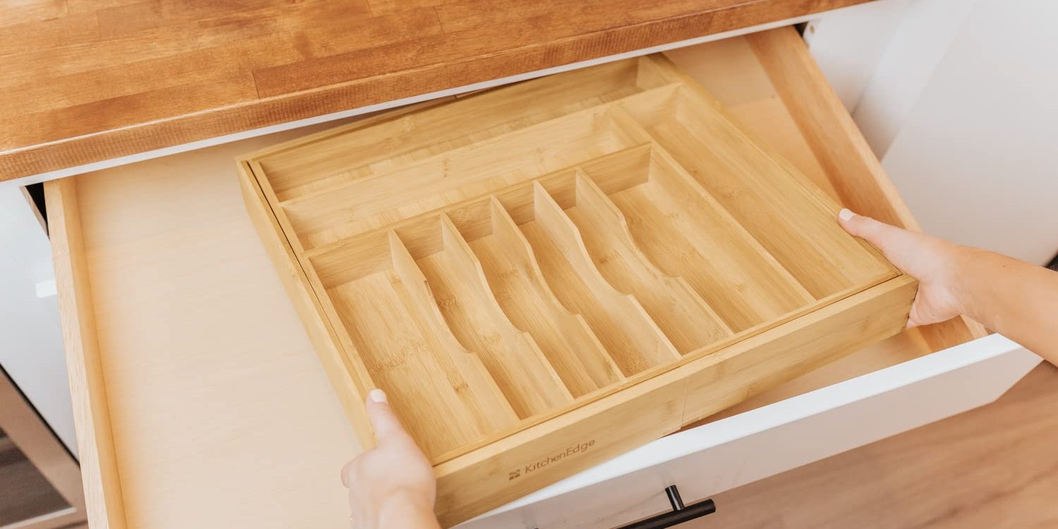 Hands lowering an empty drawer organizer into a kitchen drawer to check the fit