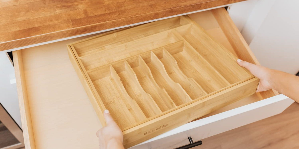 Hands lowering an empty drawer organizer into a kitchen drawer to check the fit