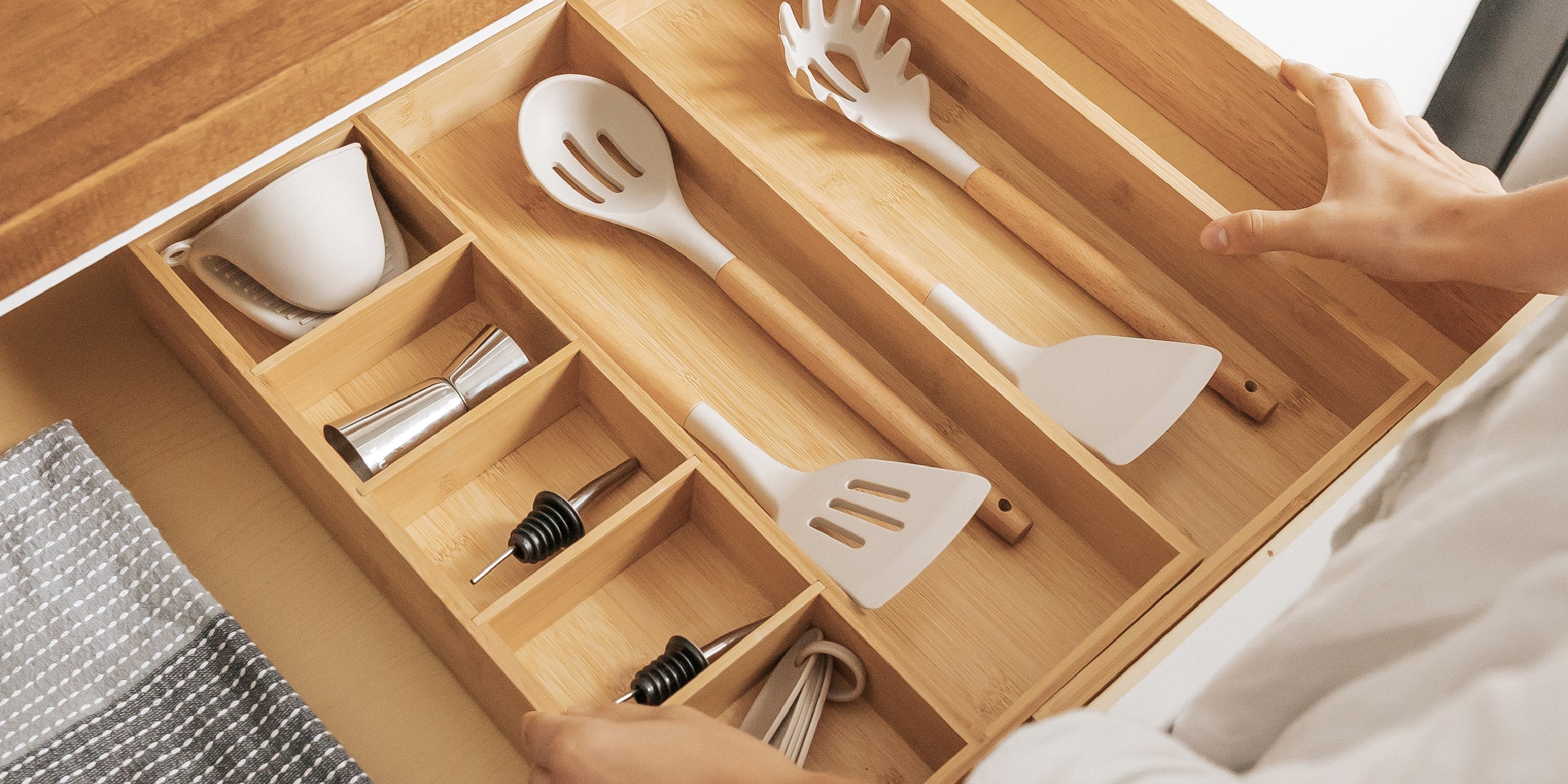 Hands seating a bamboo drawer organizer squarely in an open kitchen drawer