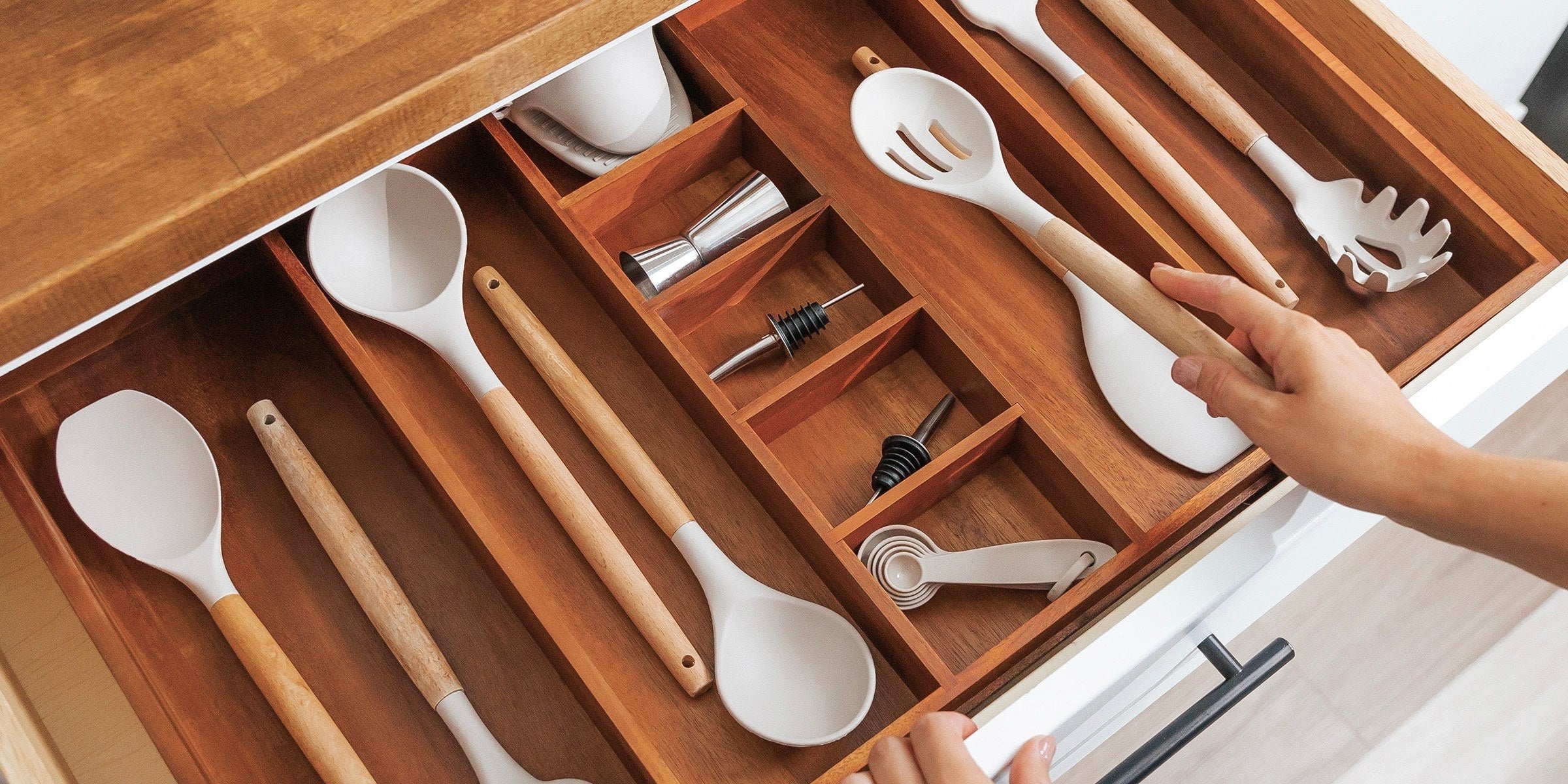 Hand placing a spatula into an acacia drawer organizer in an open kitchen drawer